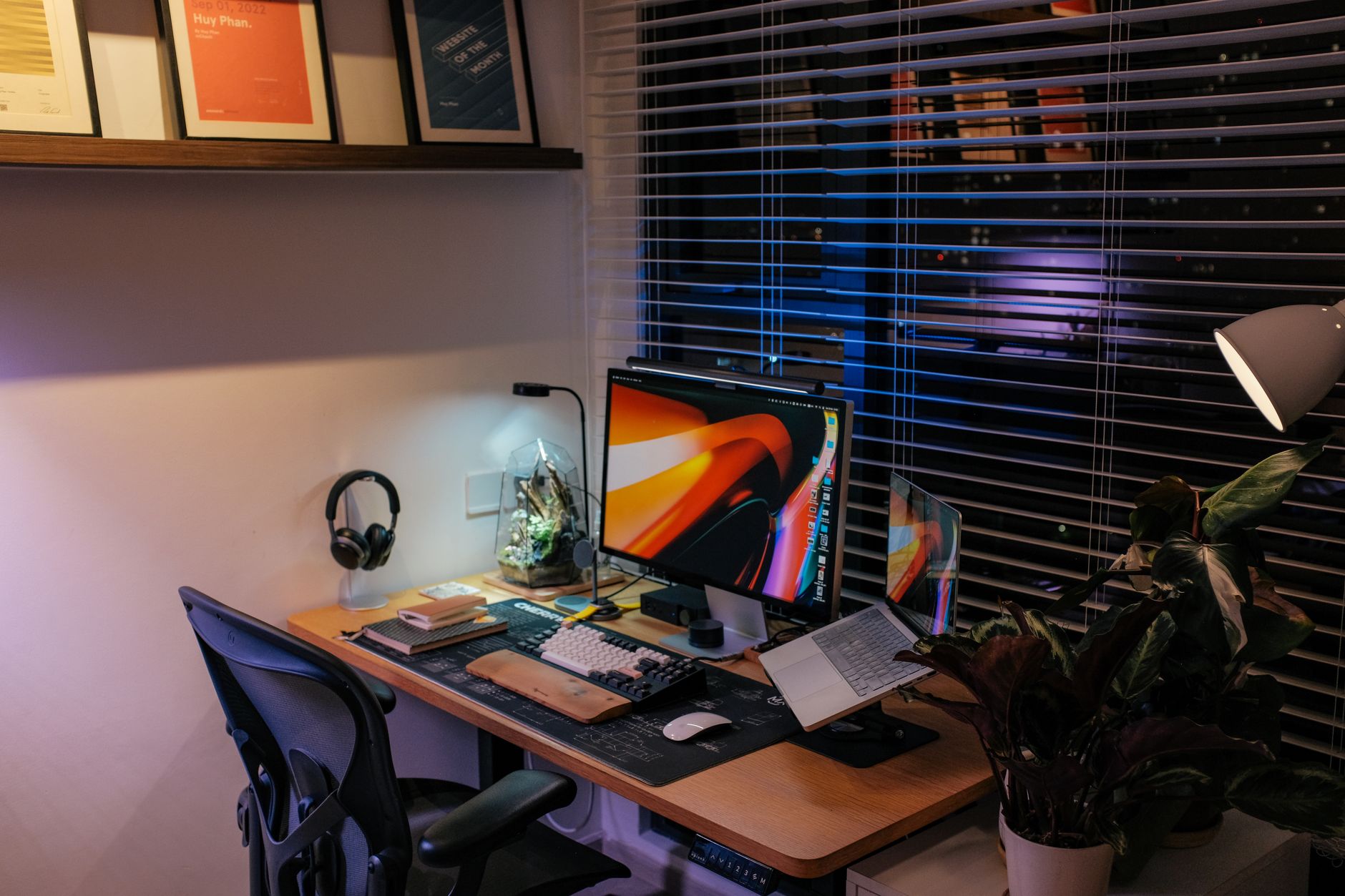 A cozy home office with a sleek computer setup, ambient lighting, and houseplants, used for client writing work.